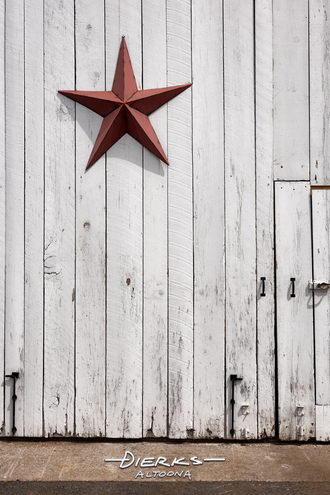 A metal barn star decoration hung high on a white barn door. In olden days, it served as a hex sign to ward off evil.