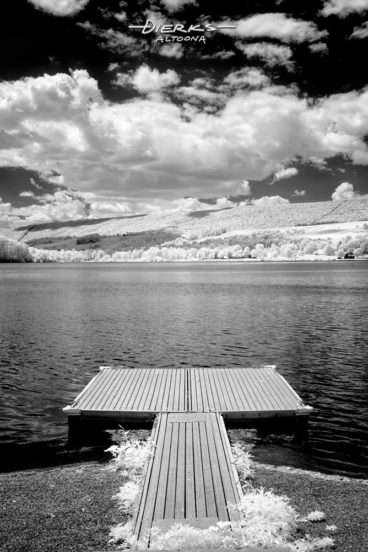 At a summer park, a lake dock under low fluffy white clouds above the water.