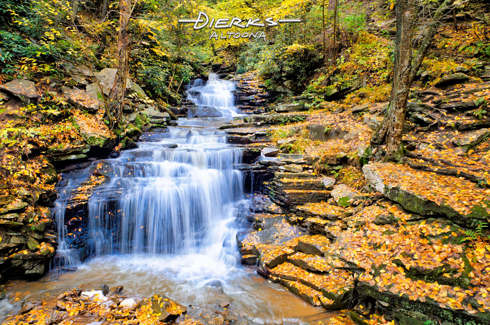 A waterfall in golden leaves of the forested Fall scenery at Rainbow Falls in Trough Creek State Park in Pennsylvania.